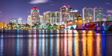 West Palm Beach skyline illuminated at night, reflected in the water, near Donald J. Trump International Airport
